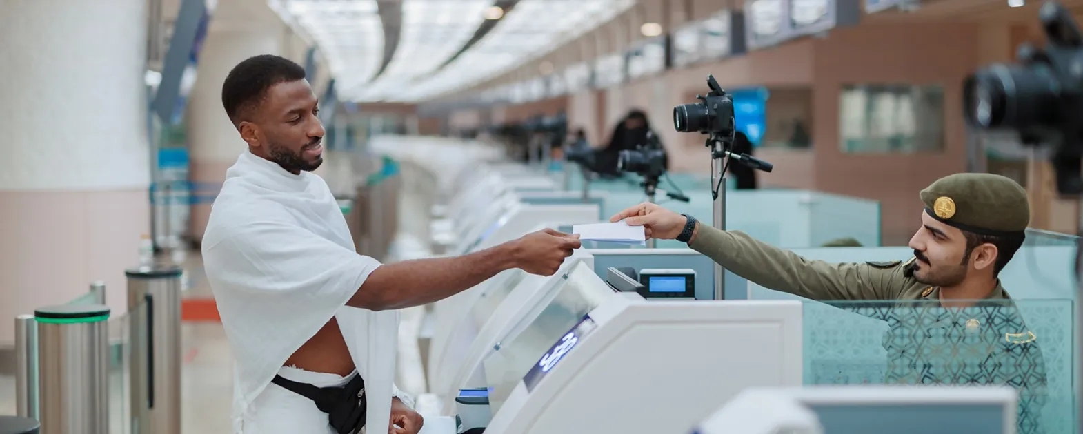  An immigration officer checking travel documents and visa information for a pilgrim in Ihram at a modern airport terminal.