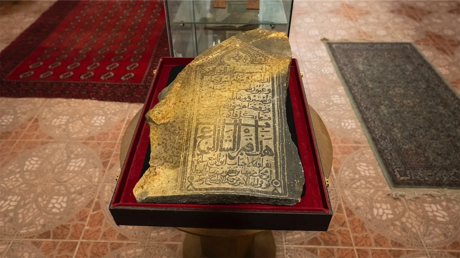 An ancient stone slab with Kufic Arabic inscriptions displayed on a red velvet cushion at The Dinar Islamic Museum in Makkah.