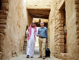 Two men standing in front of a traditional mud-brick building showcasing the historic architecture of the Makkah region.