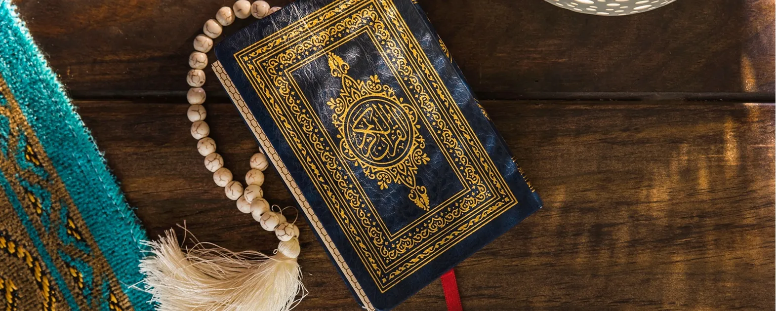 A Holy Quran book and prayer beads placed on a wooden surface, symbolizing religious tradition and culture.