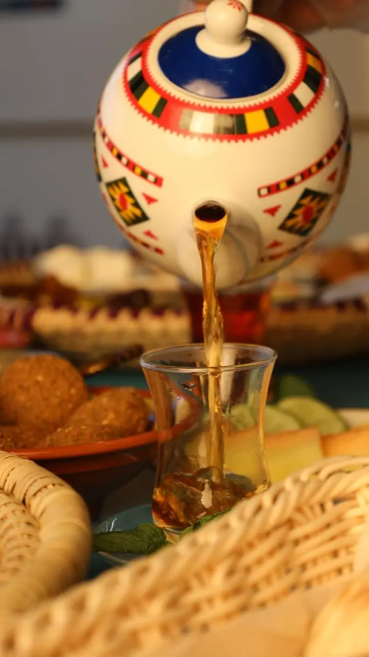 Pouring traditional tea from a decorative teapot into a glass at Shishni Restaurant in Makkah.
