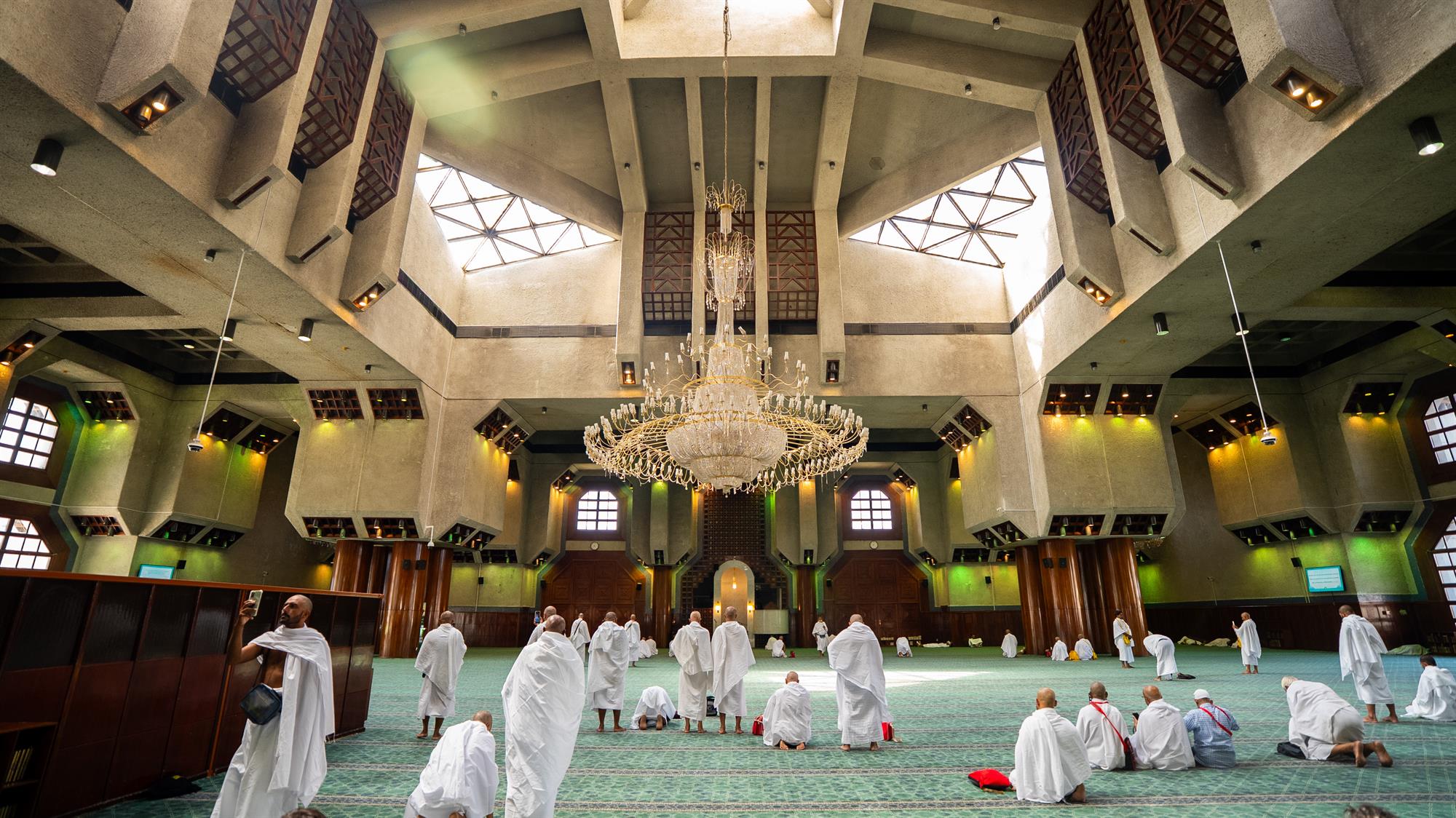 Pilgrims gathered for prayer inside the main hall of Al-Taneem Mosque in Makkah featuring unique geometric ceiling windows.
