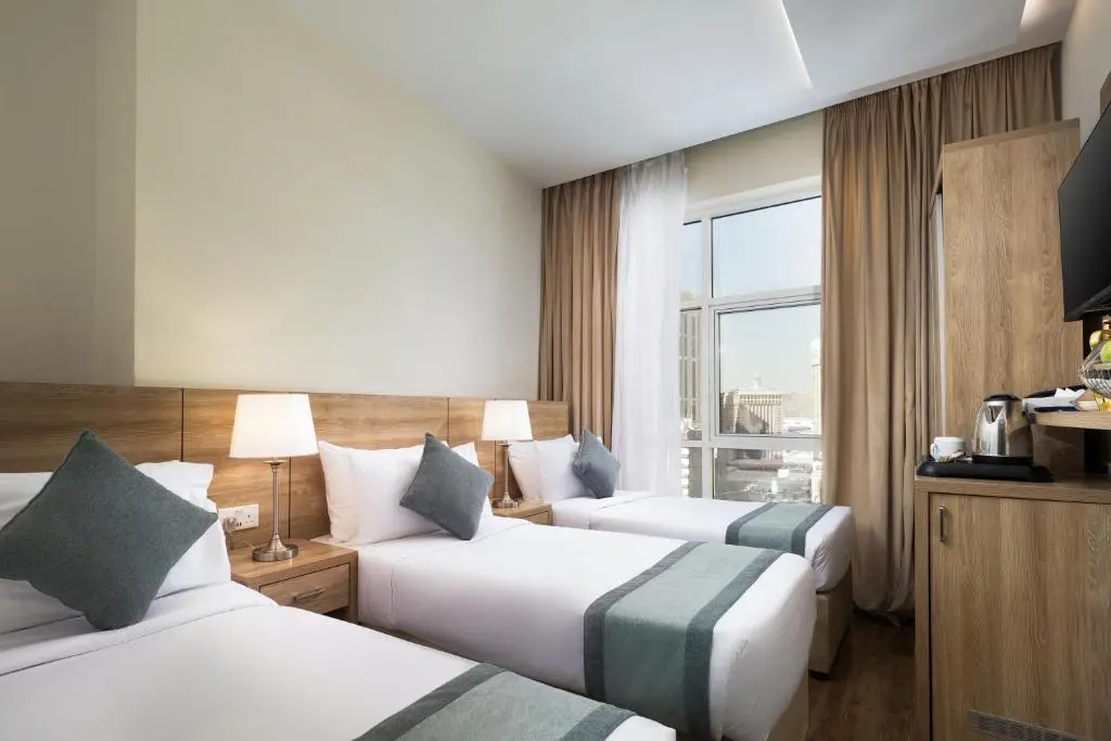 Comfortable triple bedroom interior at Emaar Worth Elite Hotel in Makkah with modern lighting and furniture.